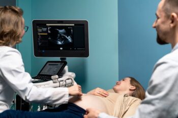Lekarz Wykonuje Badania Prenatalne Na Kobiety W Ciąży, Obok Siedzi Mąż
